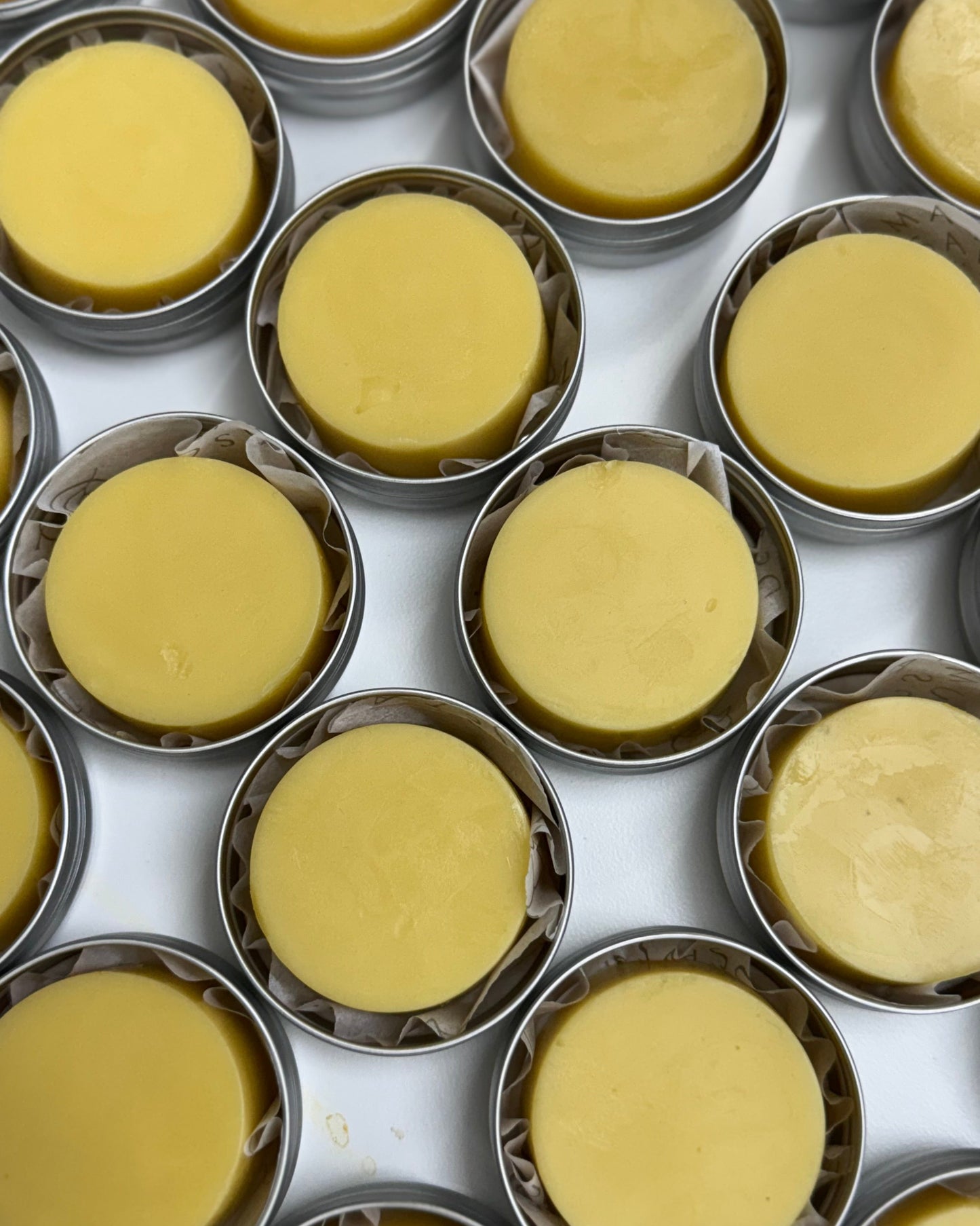 Multiple small round yellow lotion bars in metal tins on a white background


